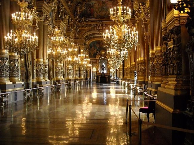 The grand foyer of the Palais Garnier, filled with chandeliers and ornate doors on the side