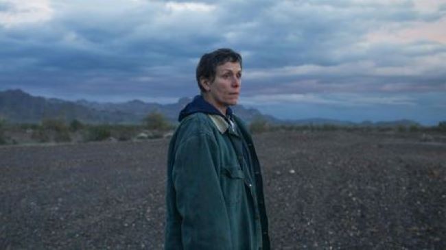A still in Nomadland from the film trailer with a lady in the middle of an American landscape