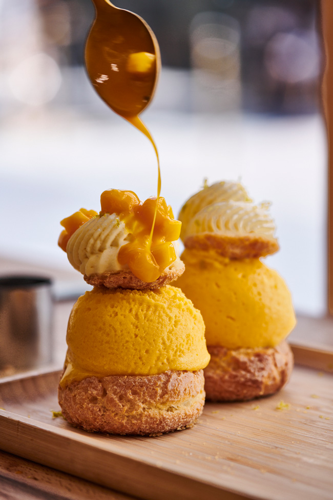 Profiterole filled with Passionfruit ice cream with whipped cream and fruit sauce with pieces of mango