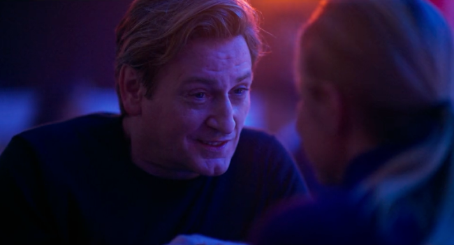 A man lit by purple lights talking to a woman