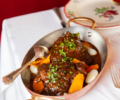 A meat dish with carrots and onions presented in a metal dish with a spoon